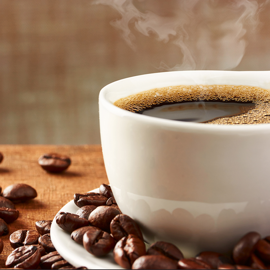 A white cup of steaming coffee with coffee beans spilled around the cup