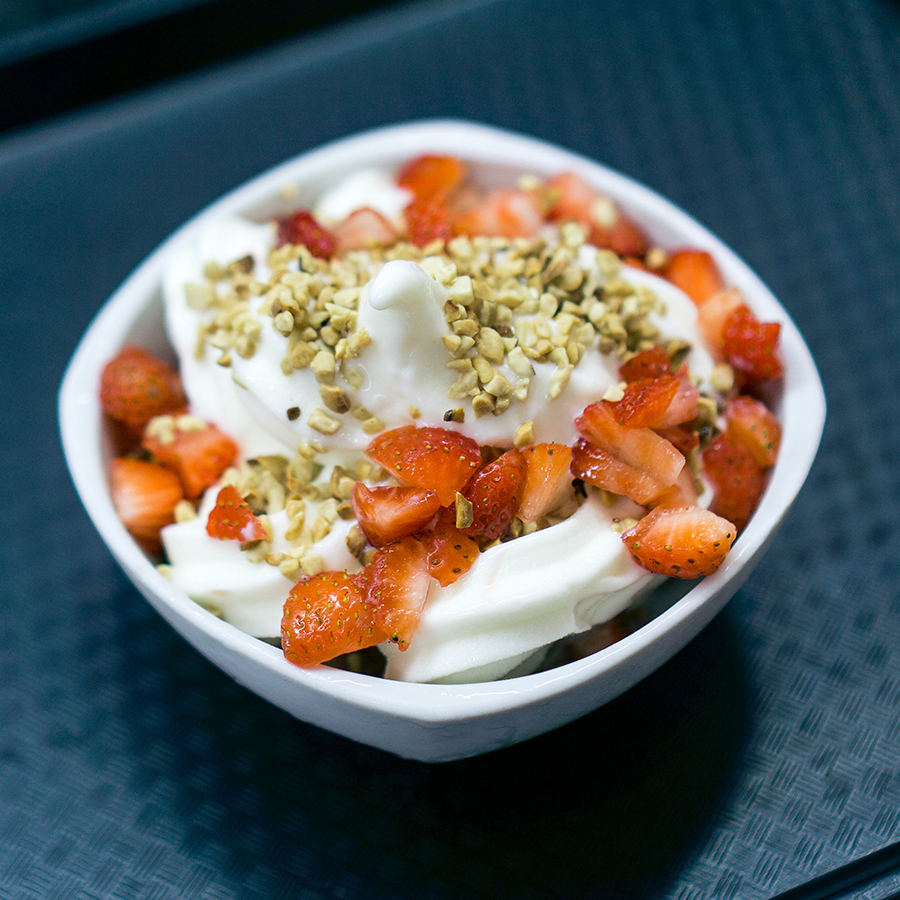 White bowl with yogurt topped with strawberries and nuts